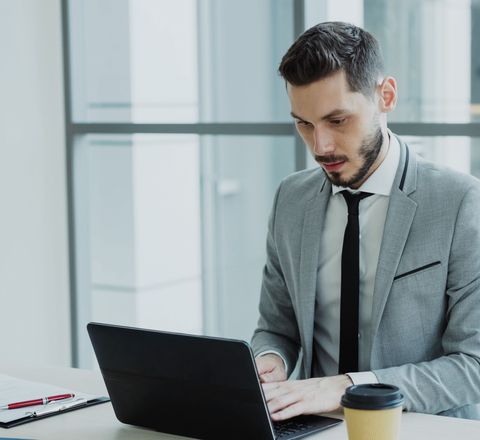 A professional at a laptop in a bright office, coffee cup on the desk