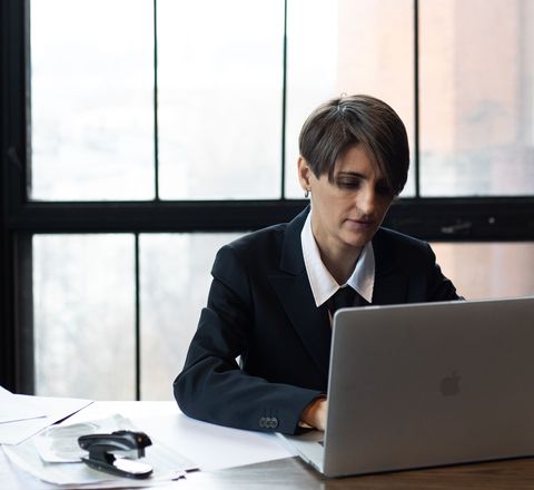 A professional working at a laptop beside a tall office window
